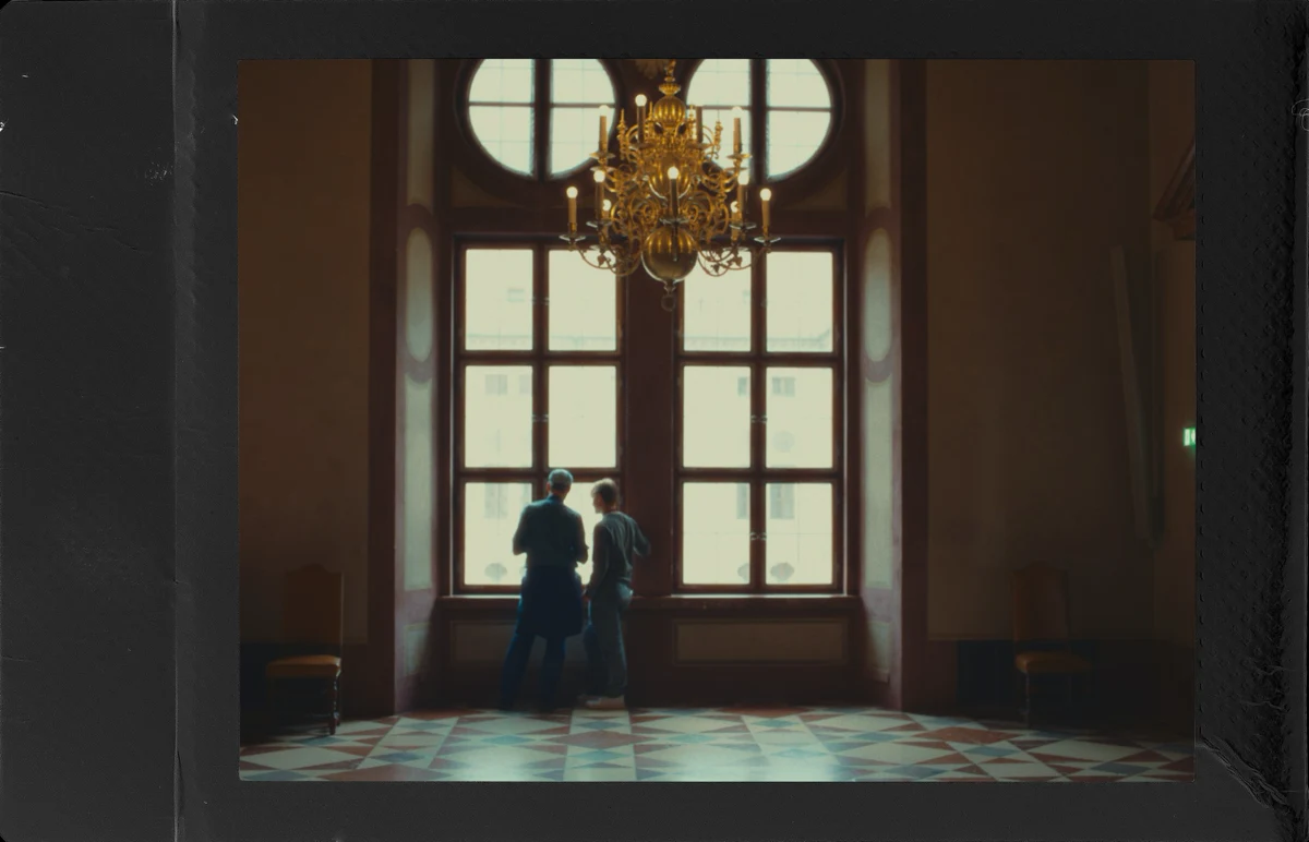 Two people beneath a chandelier in a black polaroid frame